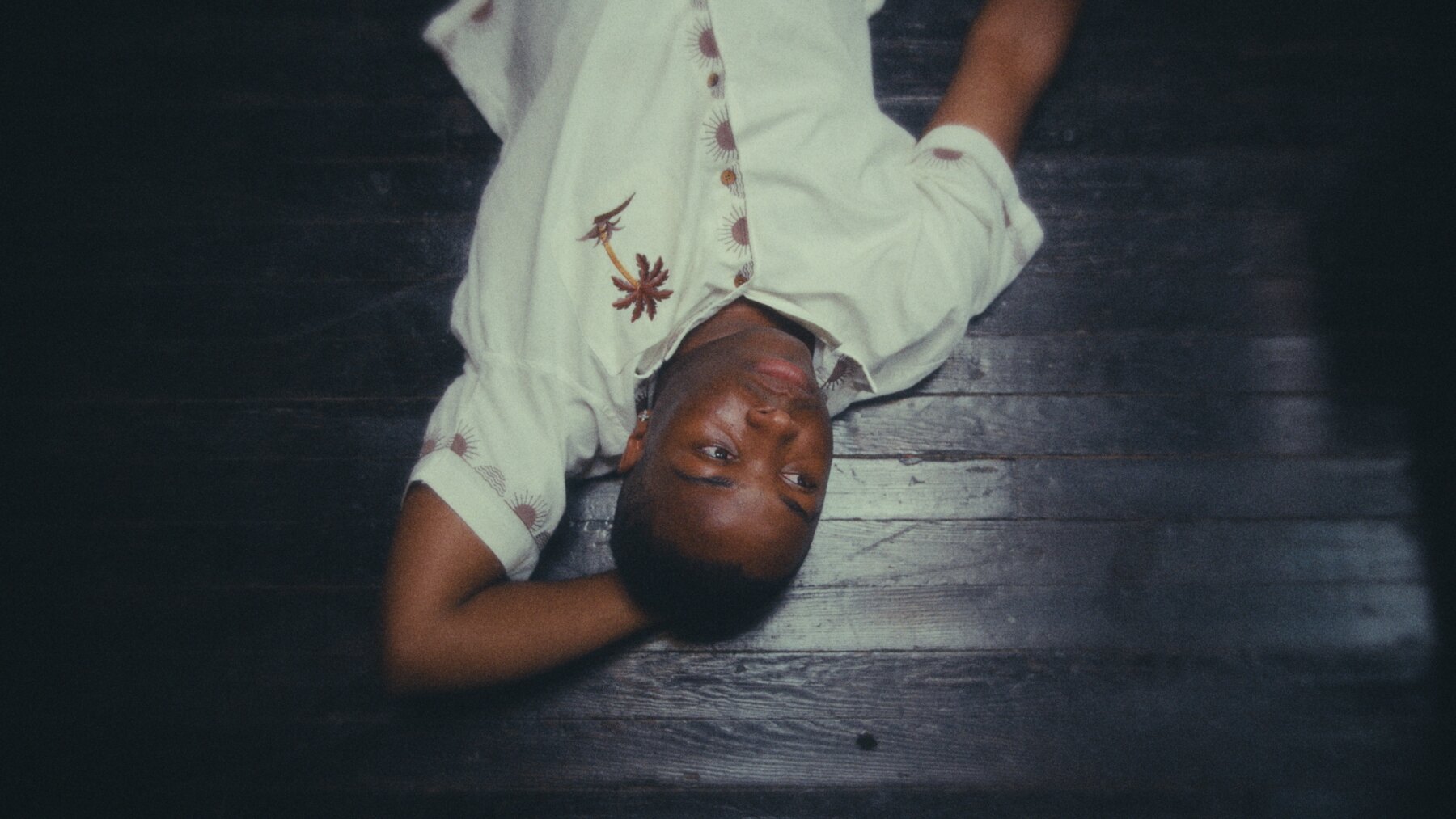 A young person lying across a dark floor in In Need of Seawater.